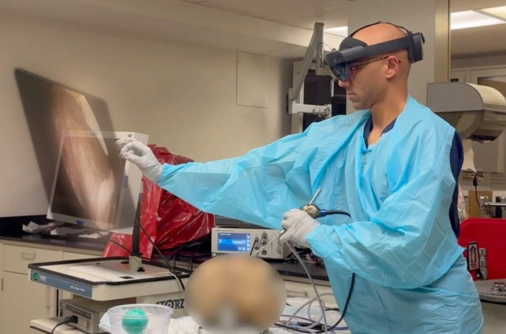 A person in medical scrubs and gloves is performing a procedure in a laboratory setting. They are using a handheld endoscopic instrument while interacting with a large monitor displaying an internal anatomical image.